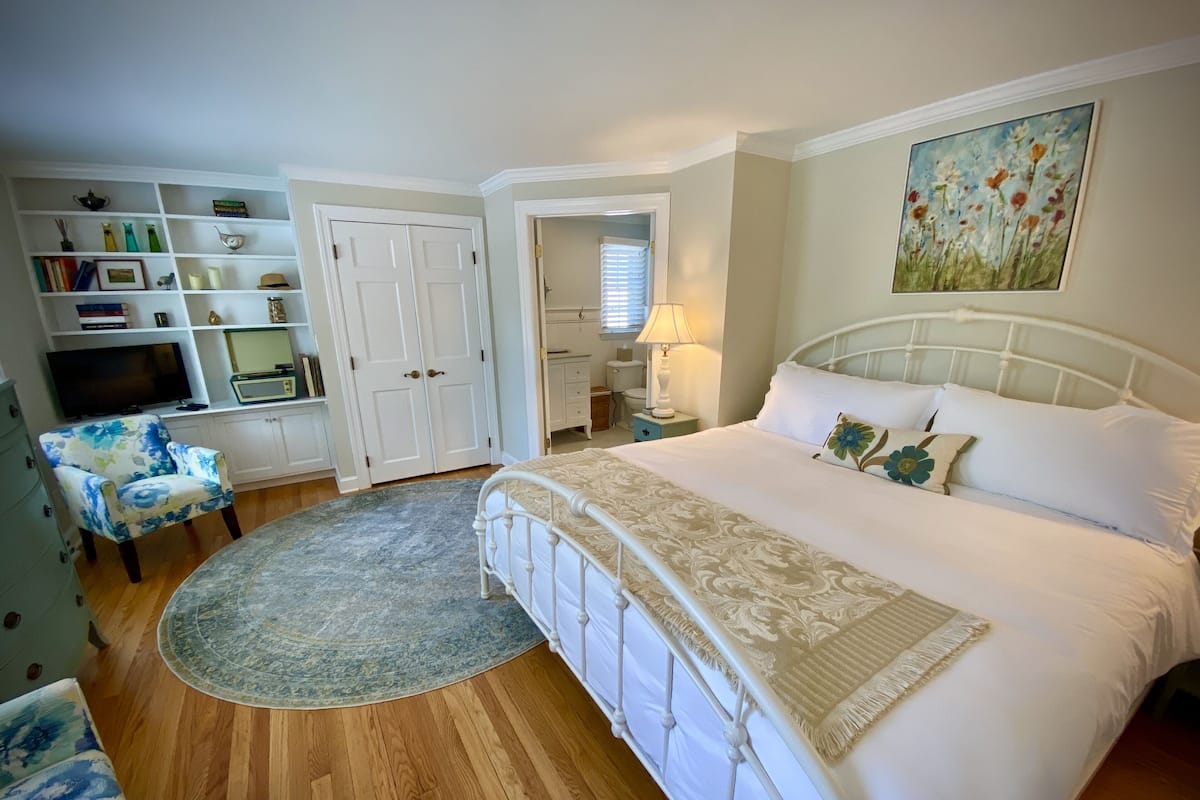 A bedroom with a bed, a chair, a TV, a wardrobe, and a painting on the wall.