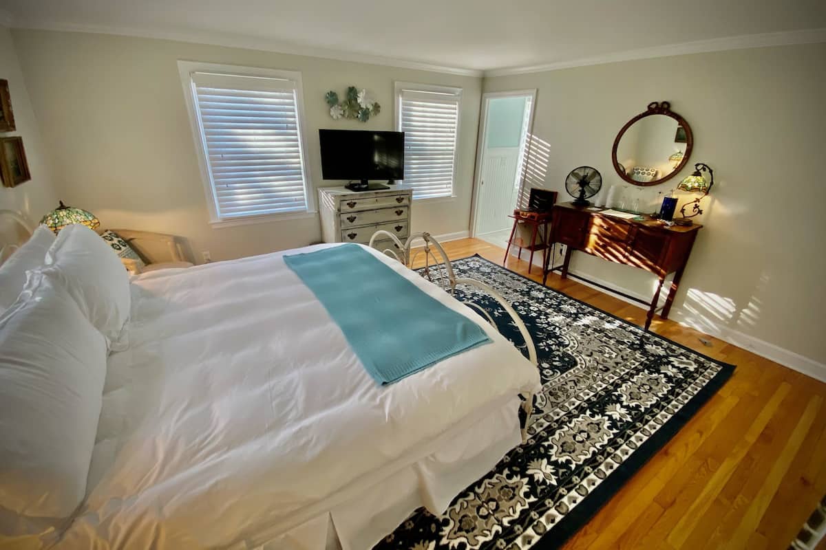 A bedroom with a large bed, a dresser, a desk, a television, and a mirror.