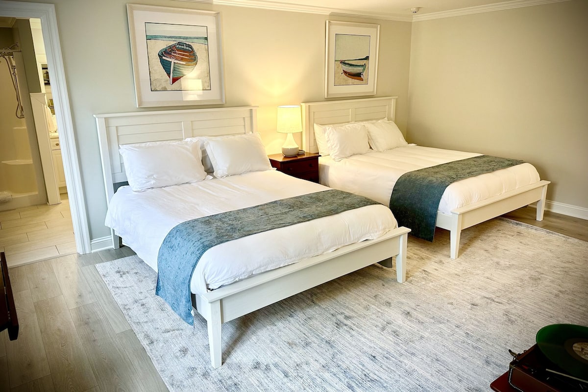 A hotel room with two beds, a white headboard, a wooden floor, and artwork on the walls.