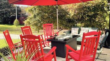 Un patio con sillas rojas, una mesa, una sombrilla y un brasero.