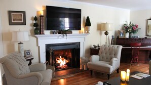 Una sala de estar con chimenea, un televisor montado encima y dos sillones.