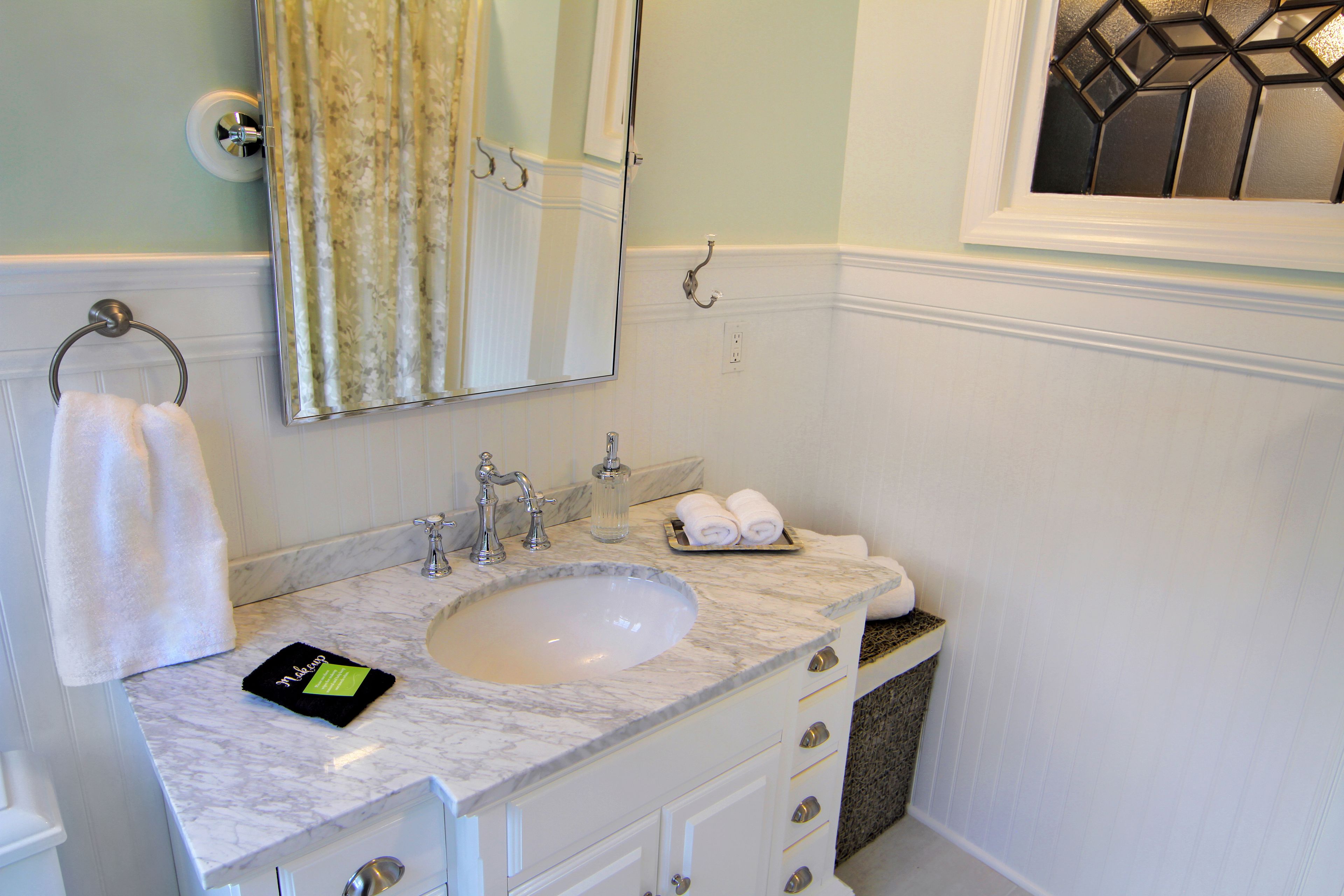 A bathroom with a marble sink, a mirror, a towel rack, and a window with a geometric pattern.