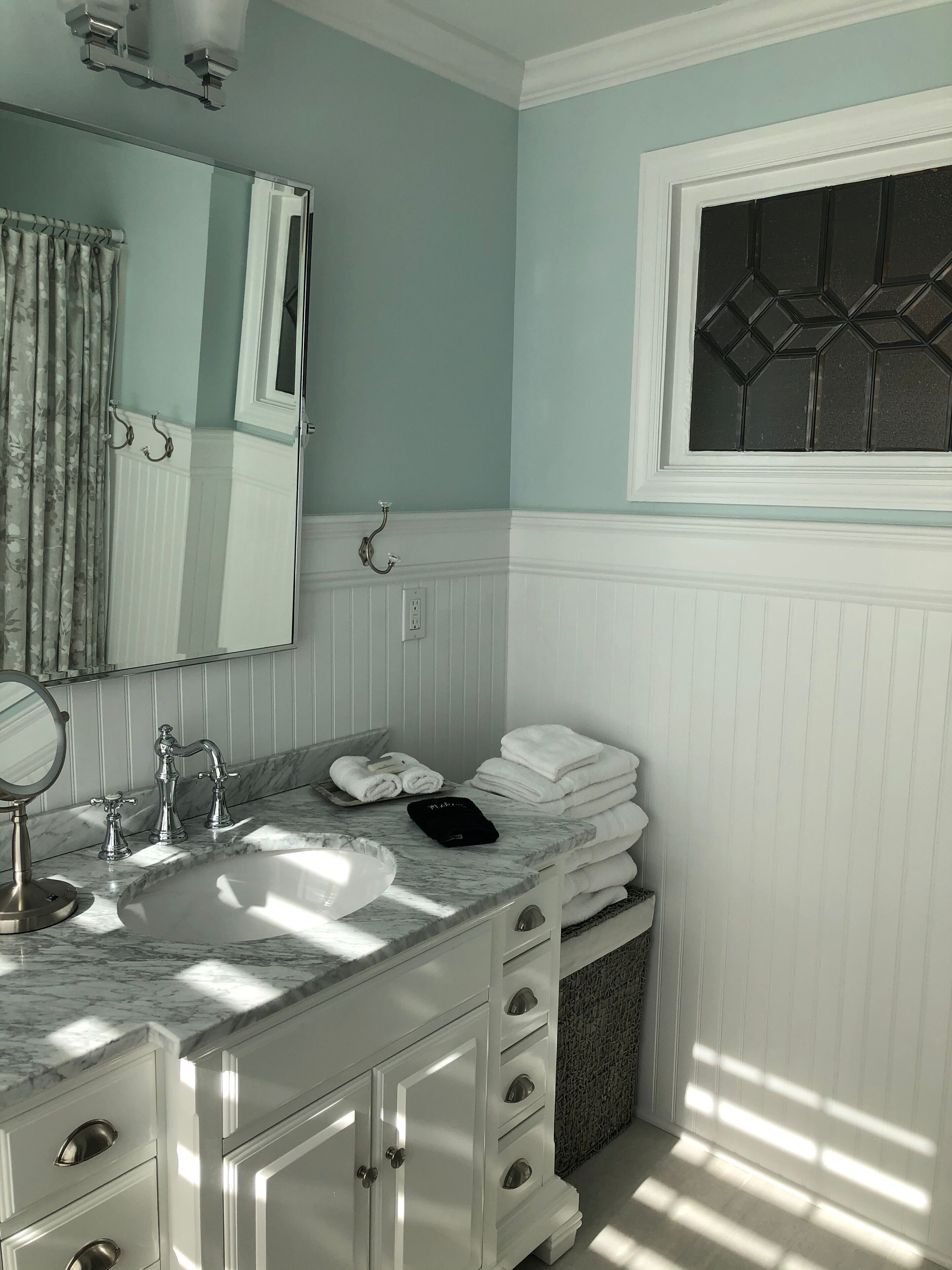 A bathroom with a marble sink, white vanity, and a mirror.
