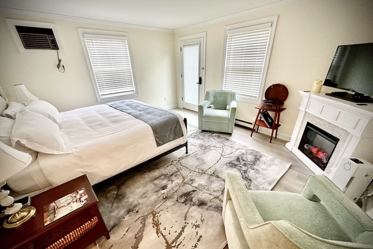 A bedroom with a bed, a chair, a fireplace, and a television.