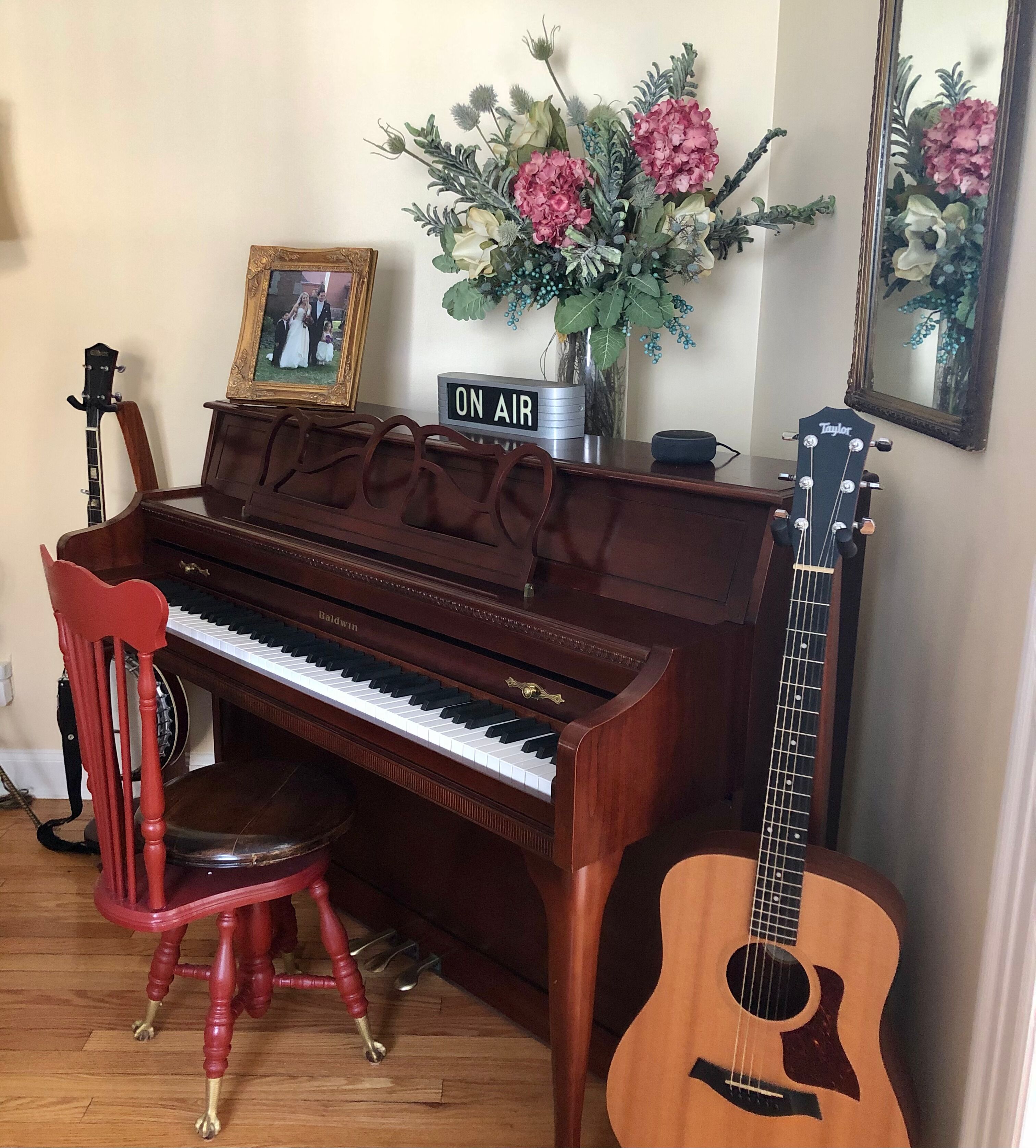 A piano, a guitar, a chair, a framed photo, and a floral arrangement on a table.