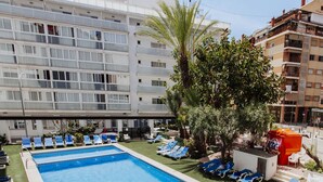 A swimming pool with blue water, surrounded by lounge chairs and palm trees. - Hotel Cuco (Benidorm)