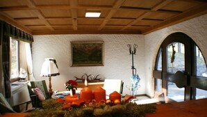 A cozy room with a wooden ceiling, a fireplace, a table with candles, and a window with a view. - Berghotel Maderhalm (Fischen im Allgaeu)