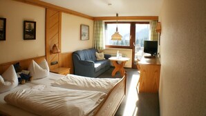 A hotel room with a bed, a sofa, a TV, and a window with a view. - Berghotel Maderhalm (Fischen im Allgaeu)