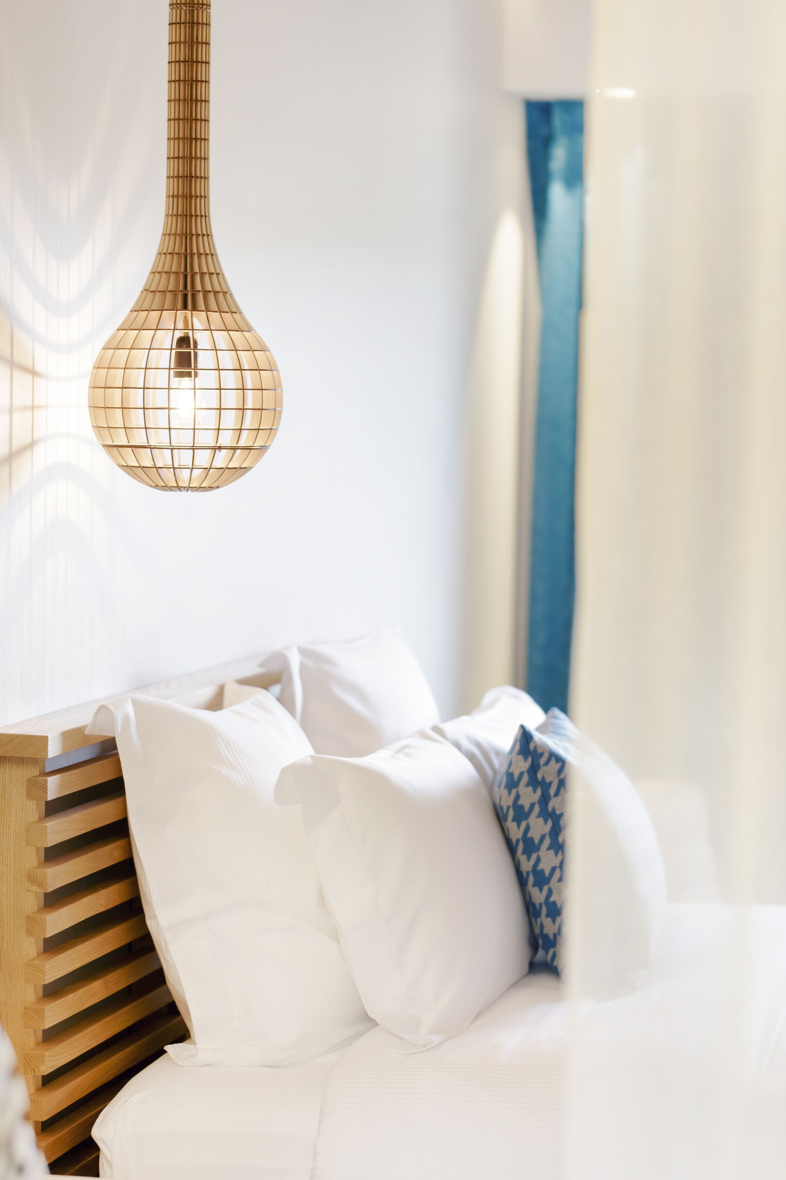 Een slaapkamer met een houten hoofdeinde, wit beddengoed en een hanglamp.