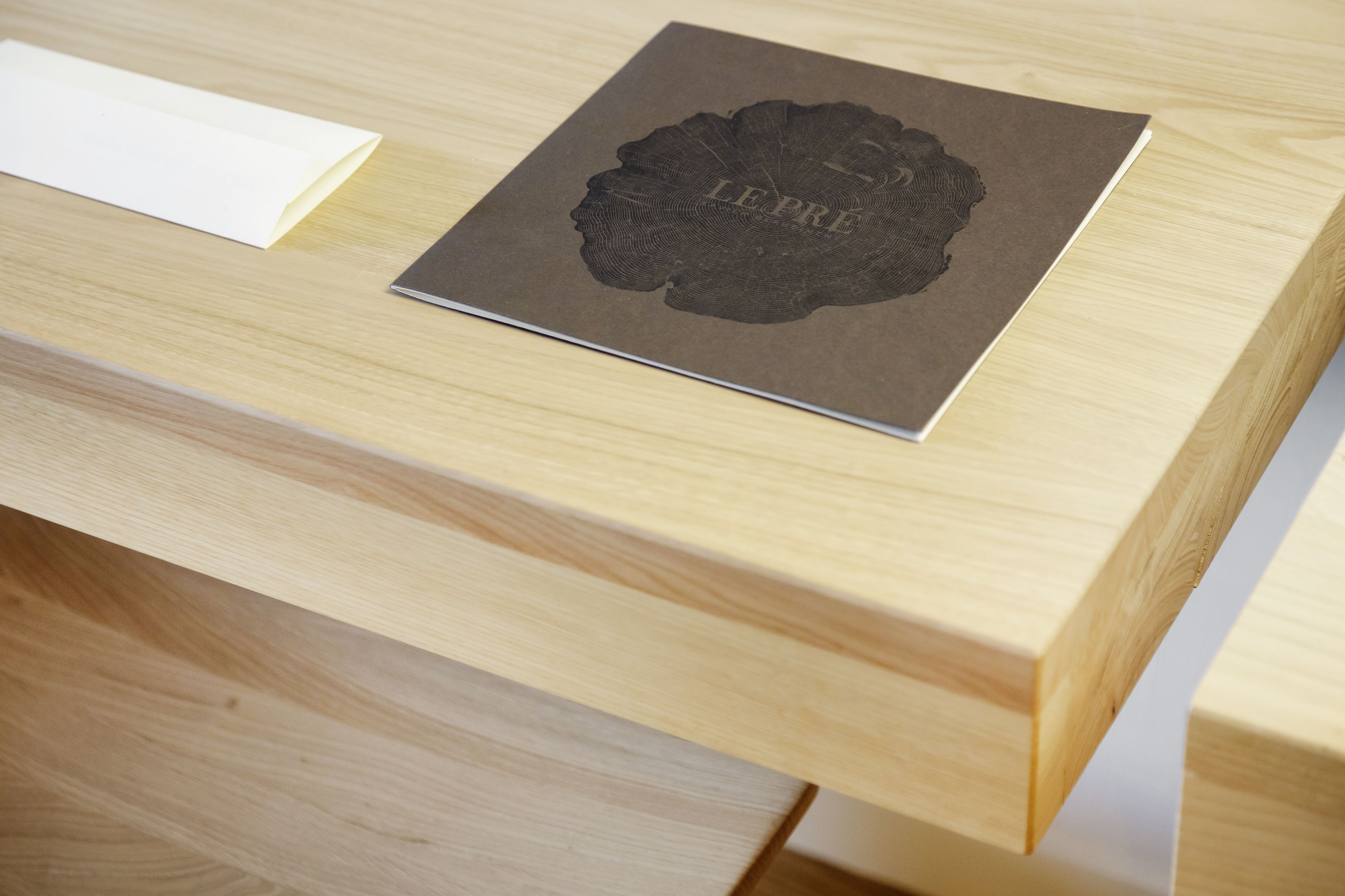 A wooden table with a dark-colored folder labeled "LE PRE" on top.