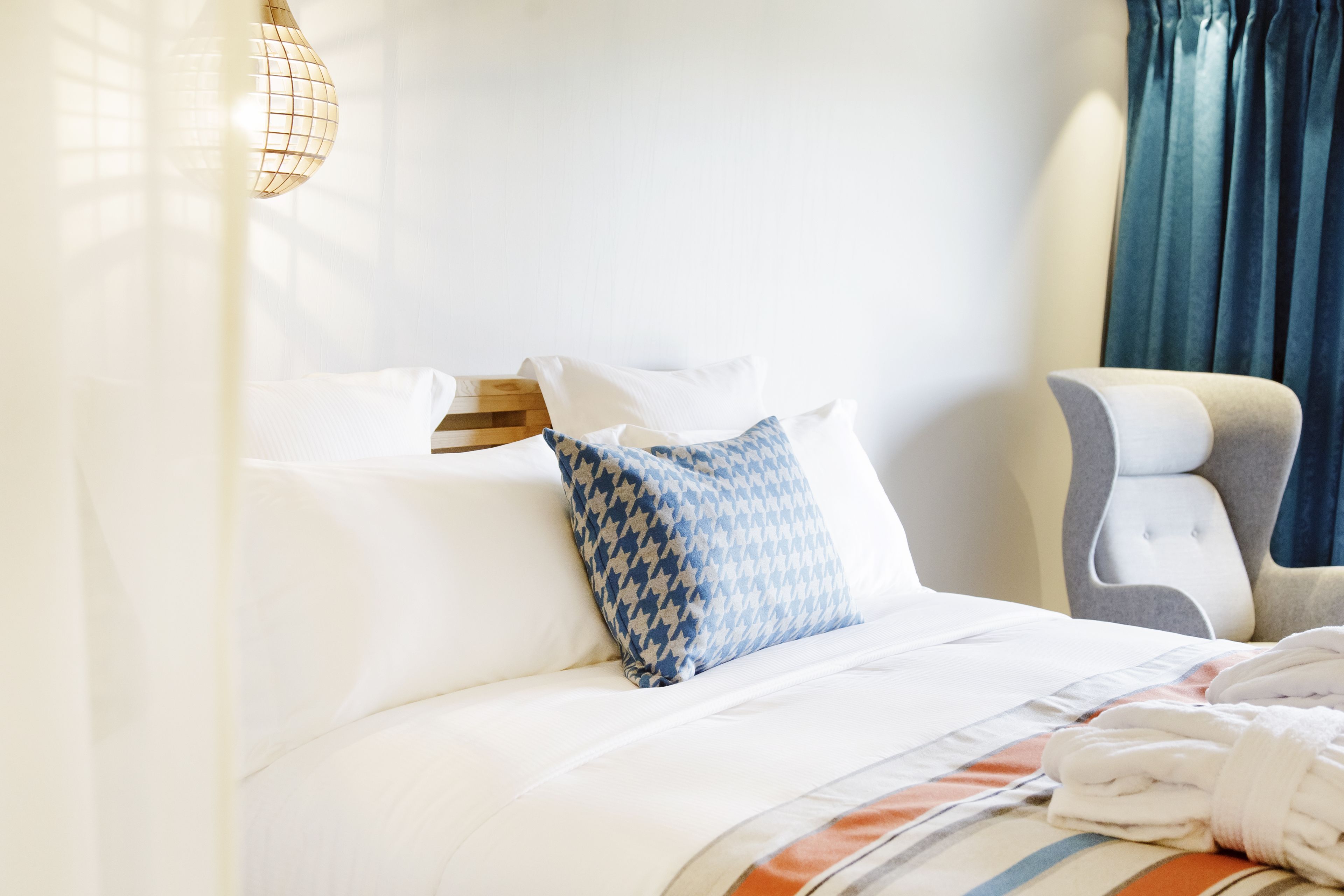 A hotel room with a neatly made bed, a headboard, a chair, and a lamp.