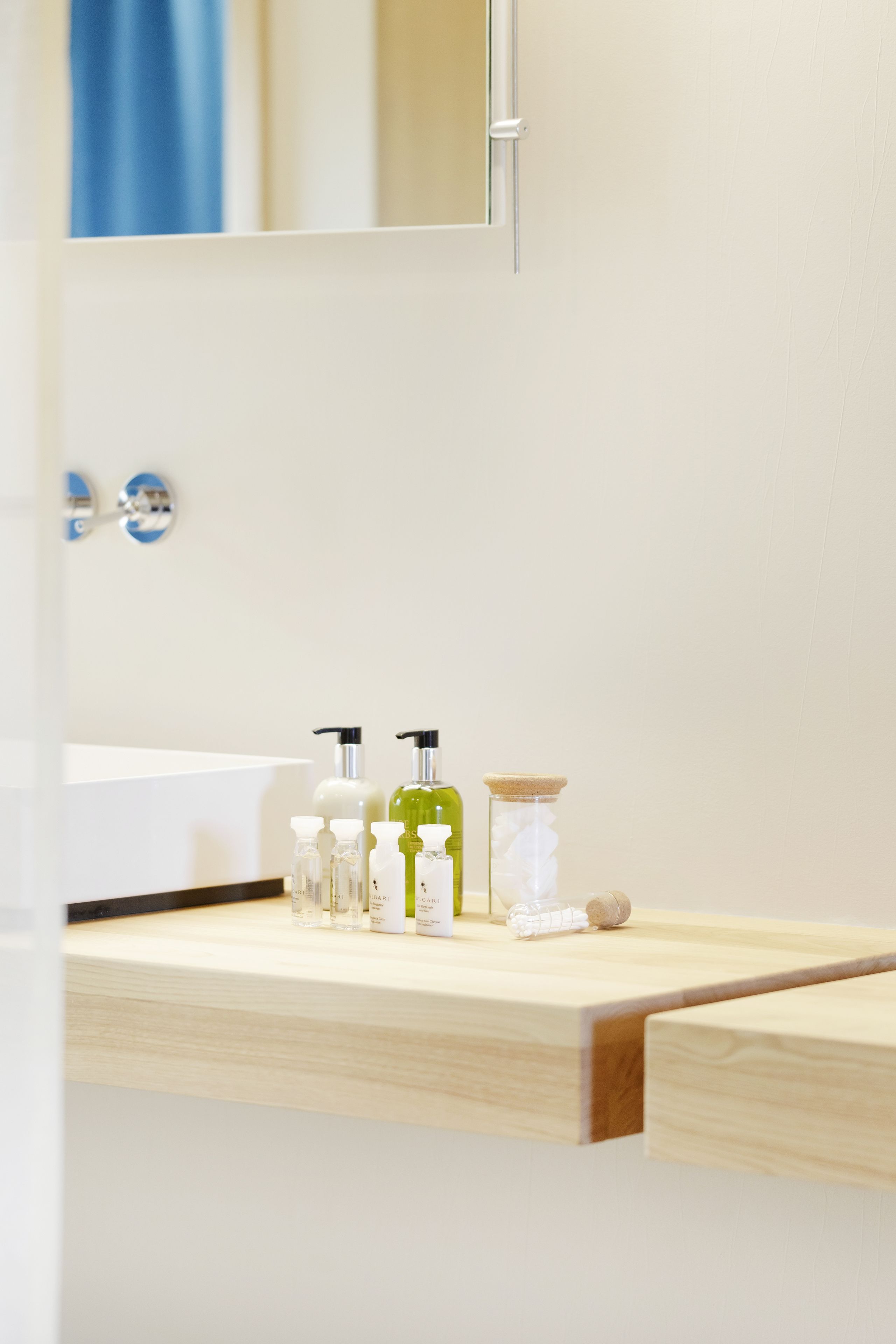 A bathroom with a white sink, mirror, and wooden countertop. There are several toiletries on the counter, including a green bottle, a white bottle, and a clear bottle.