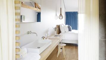 Une salle de bain moderne avec un grand miroir, un lavabo blanc et un tabouret en bois.