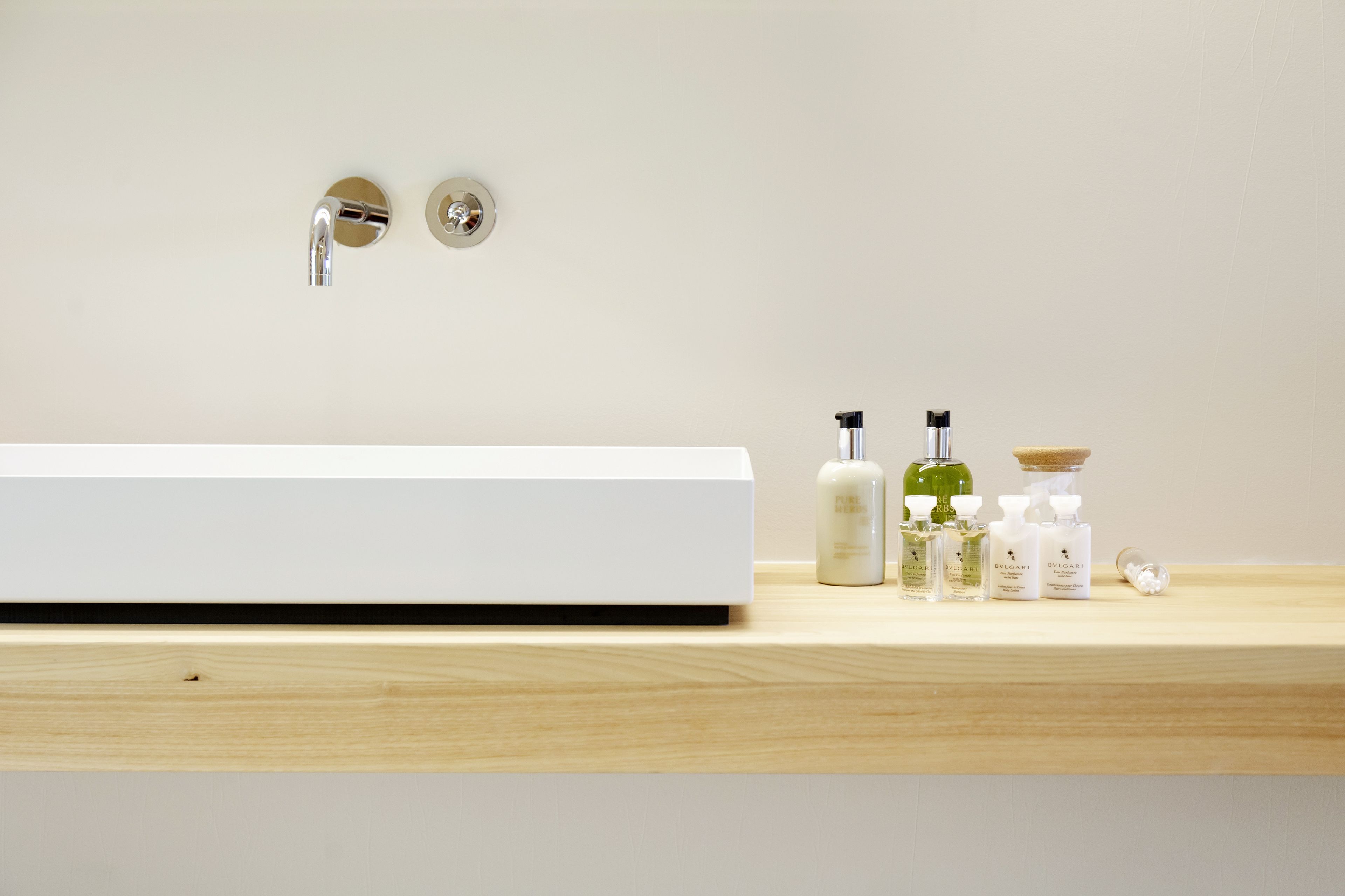 Un baño moderno con un lavamanos blanco, dos grifos y una encimera de madera.