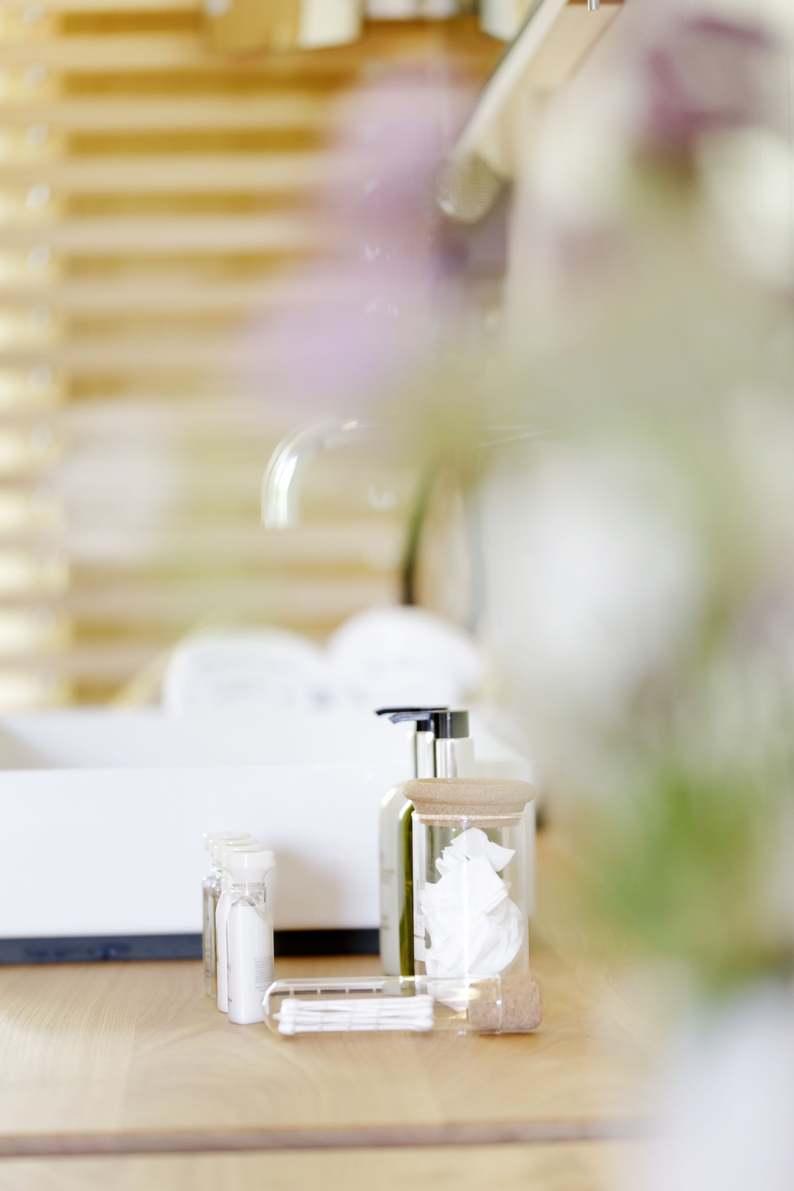 A bathroom with a wooden vanity, a mirror, and various toiletries including a bottle of lotion and a glass container with a white substance.