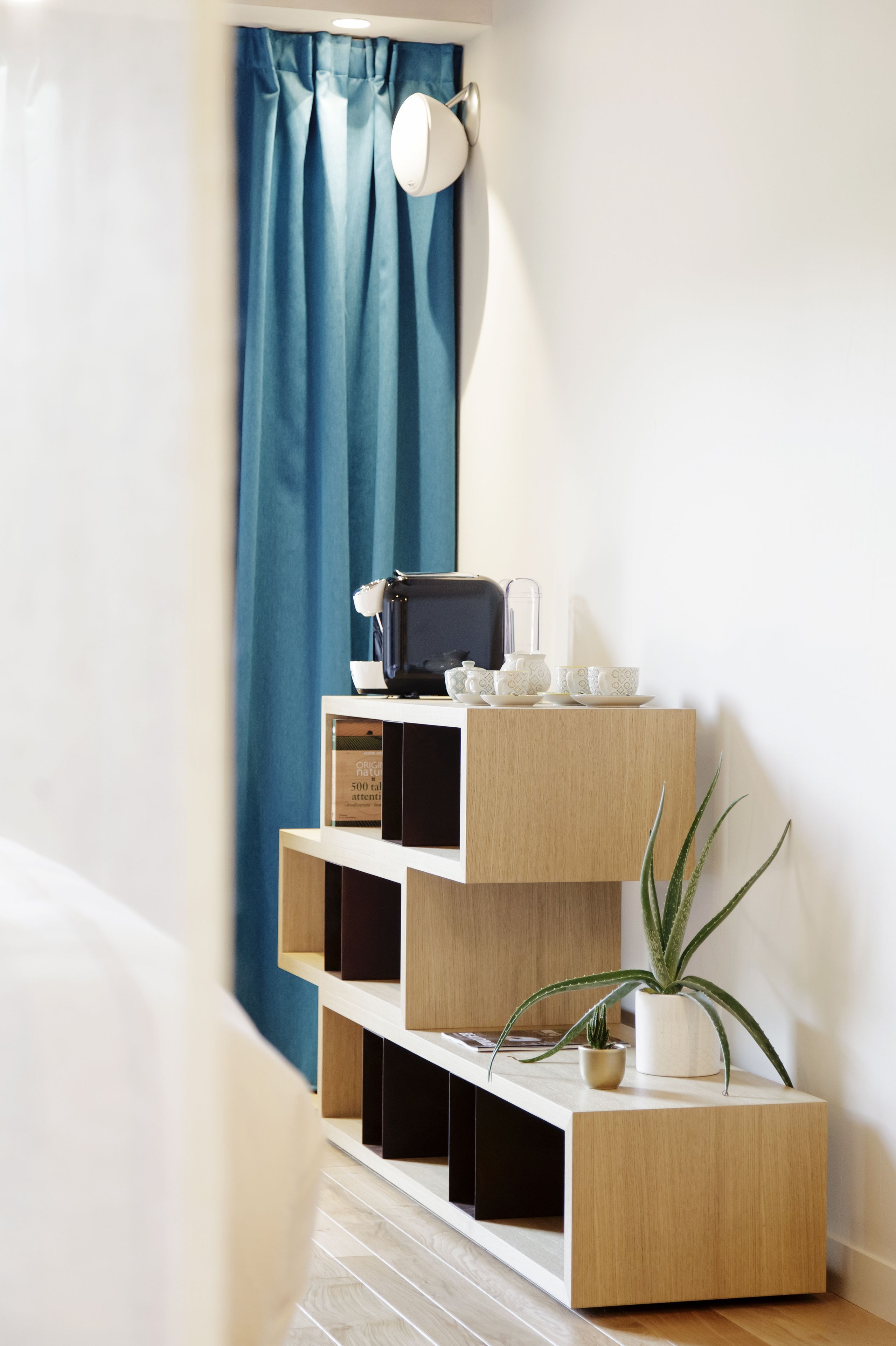 Un coin avec un rideau bleu, un mur blanc et une étagère en bois sur laquelle est posée une plante.