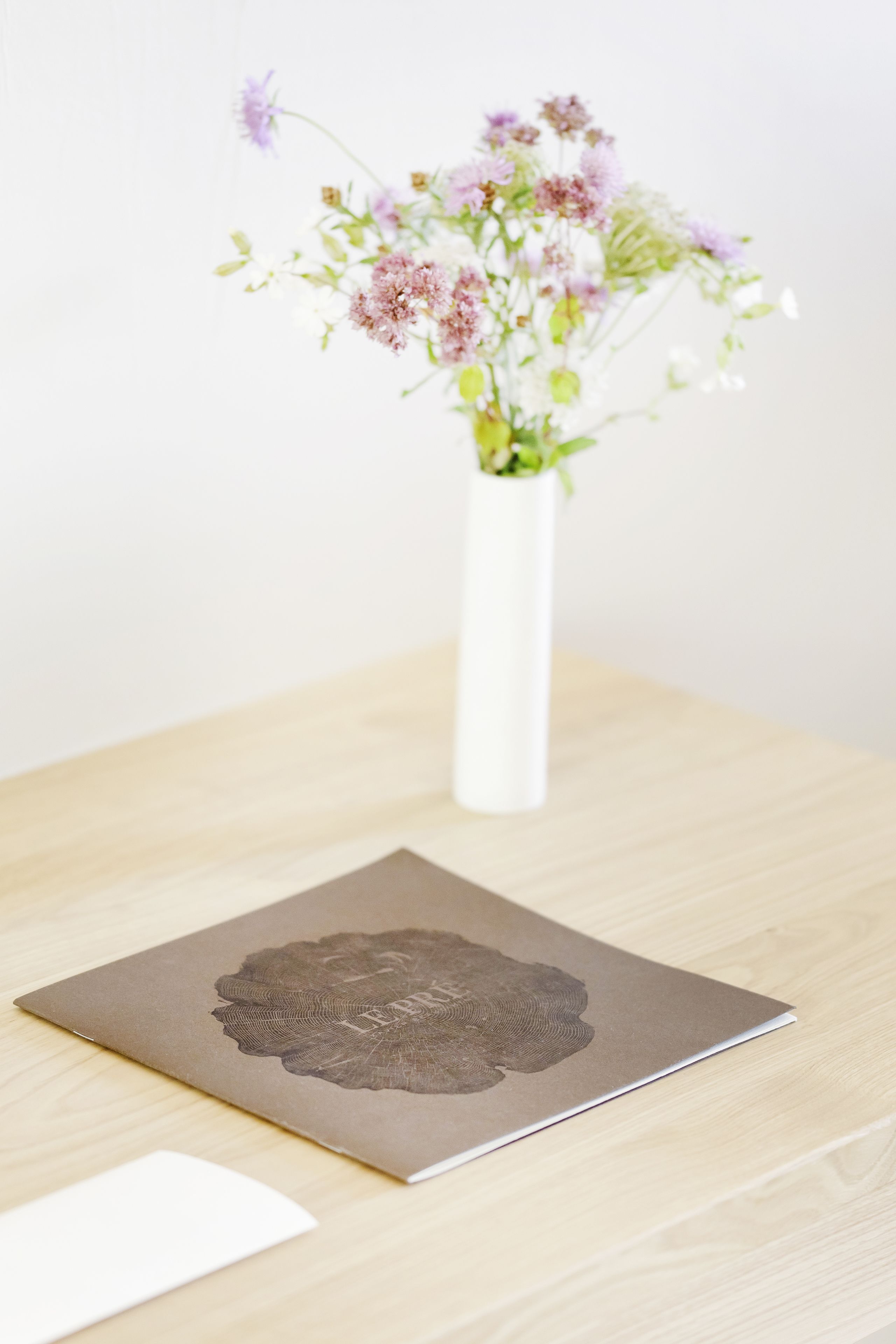 A white vase with flowers on a wooden table.