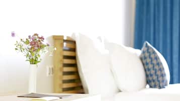 Un dormitorio ordenado con una mesita de noche que sostiene un jarrón de flores, un libro y un teléfono inteligente.