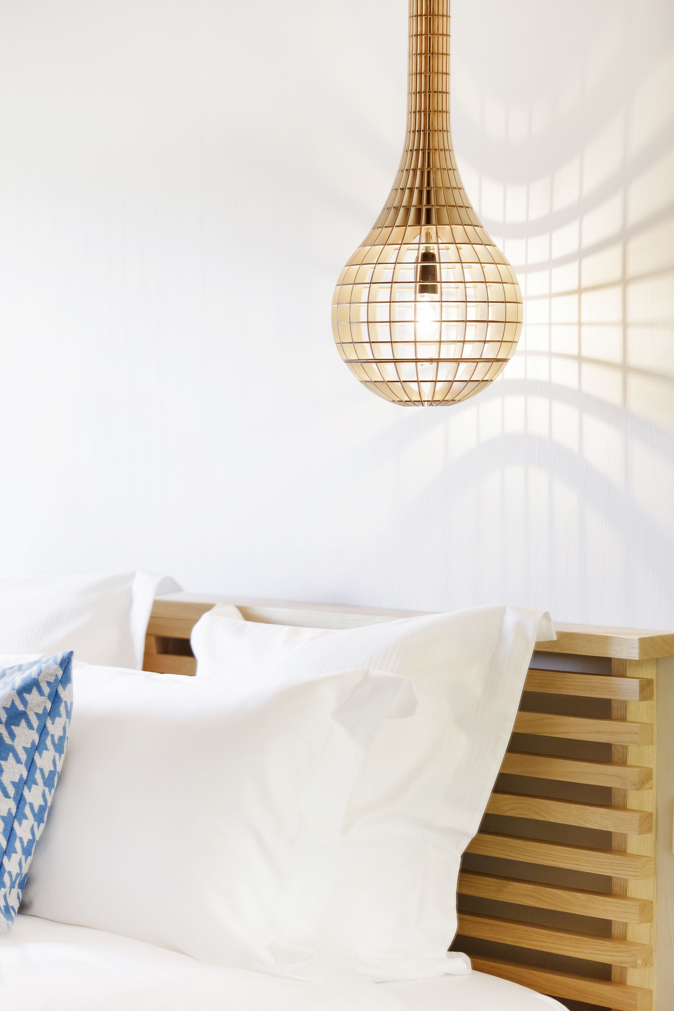 Een bed met witte beddengoed en een kussen met blauw patroon, een houten hoofdbord en een hangende lamp.