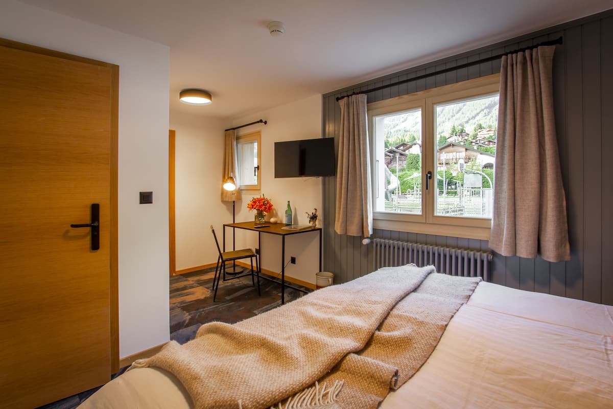 Ein Hotelzimmer mit Bett, Schreibtisch, Stuhl, Fernseher und einem Fenster mit Vorhängen.