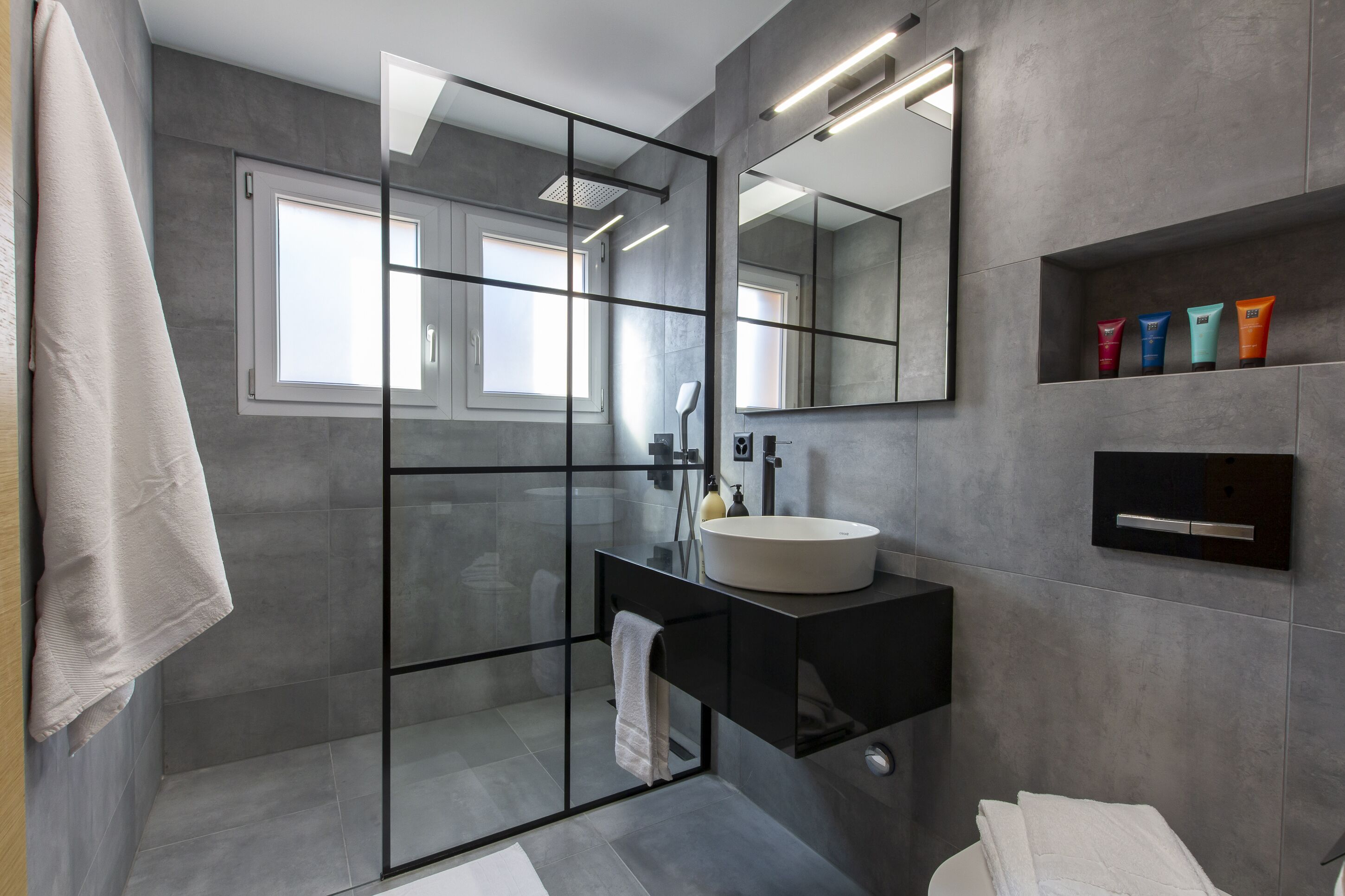 A modern bathroom with a glass-enclosed shower, a large mirror, and a vanity with a sink and towel rack.