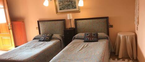 A hotel room with two single beds, a small round table, a framed picture on the wall, and a door with curtains.
