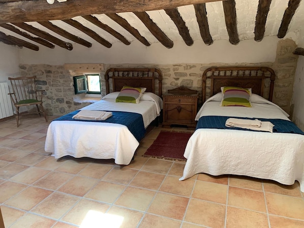 A room with two beds, a stone wall, a wooden chair, and a window.