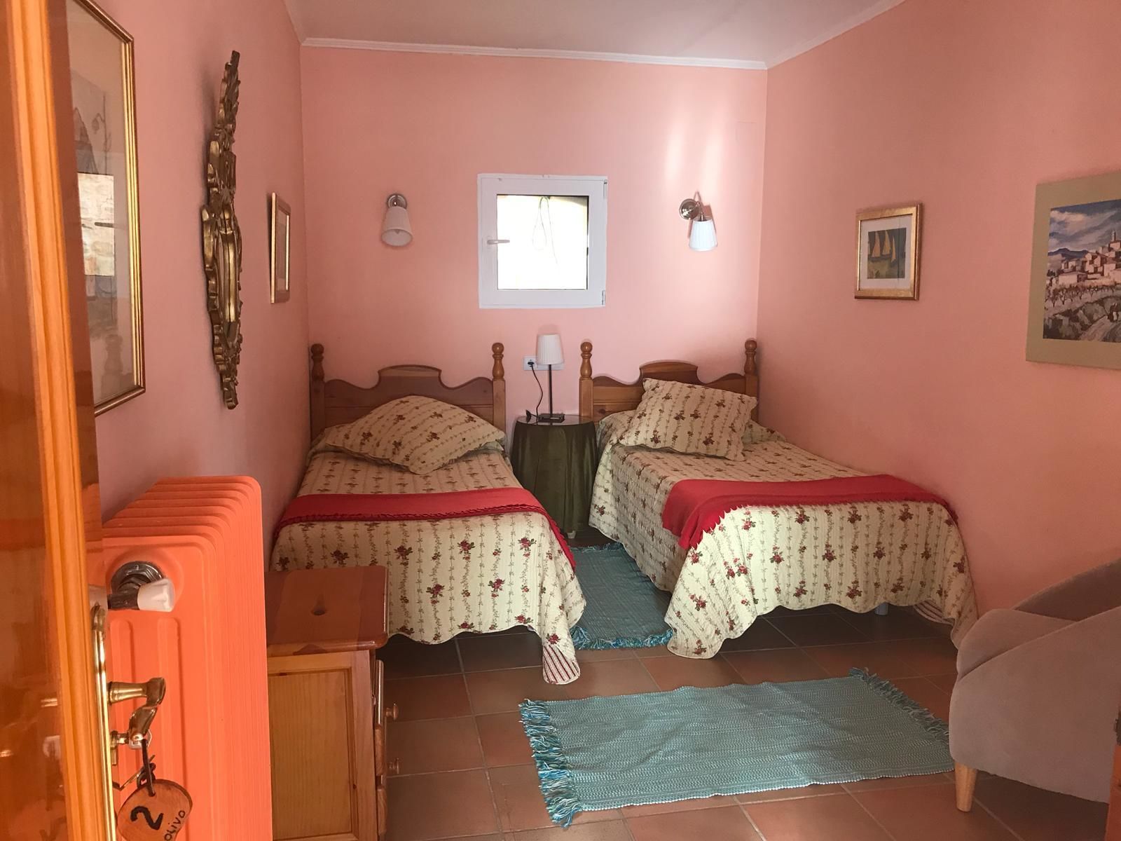 A bedroom with two beds, a window, a door, and a small table.