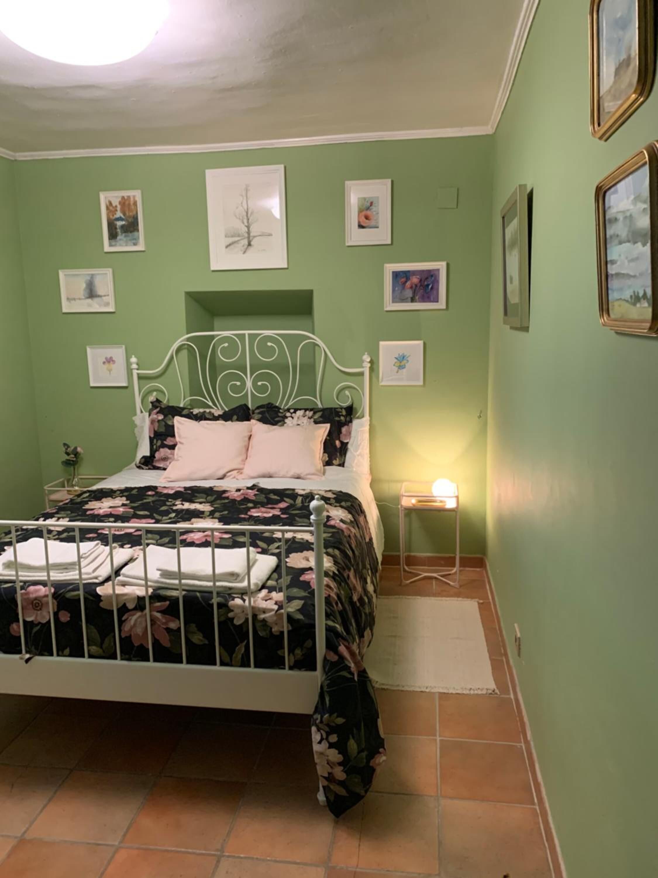 A bedroom with a bed, a nightstand, and a wall with framed pictures.