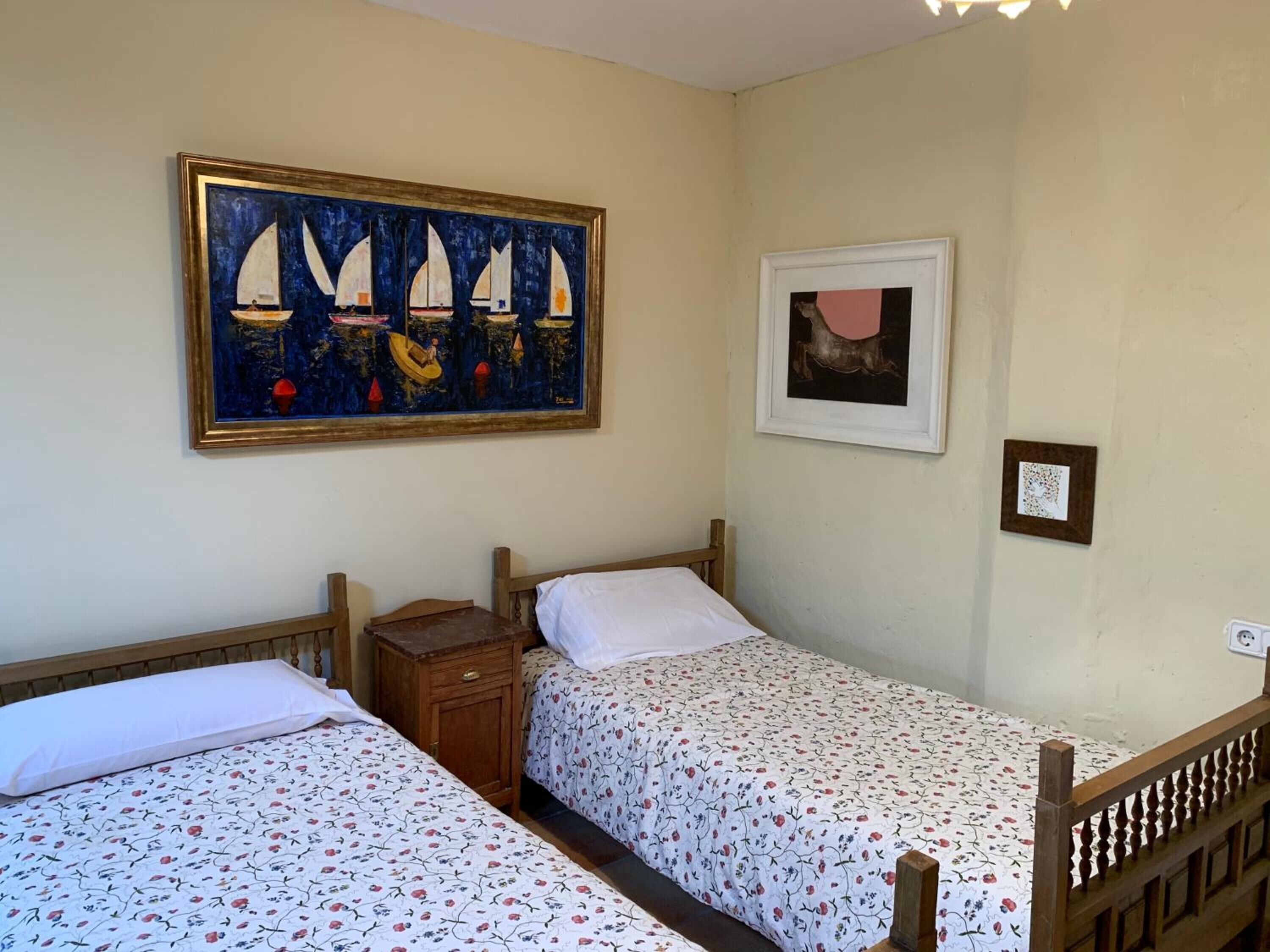 Una habitación con dos camas individuales, una mesita de noche y un cuadro de veleros.