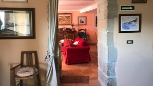 Una sala de estar acogedora con un sofá rojo, una silla de madera y una pared de piedra. Hay cuadros enmarcados en las paredes y una señal direccional verde.