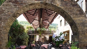 Un patio al aire libre con mesas y sillas, un arco y la vista de un edificio al fondo.