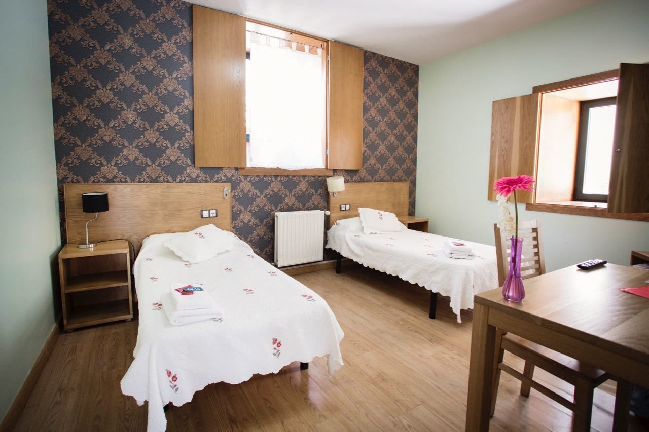 Ein Zimmer mit zwei Einzelbetten, einem hölzernen Nachttisch mit Lampe, einem Tisch mit einer Vase und einem Spiegel.