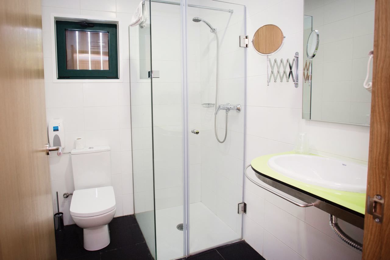 A bathroom with a glass-enclosed shower, a toilet, a sink with a mirror, and a window above the toilet.