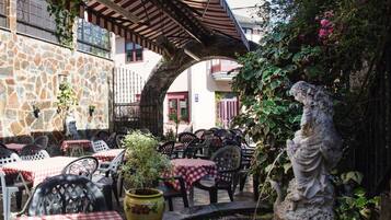 Patio esterno con pareti in pietra, tavoli a scacchi rossi e bianchi e una statua.