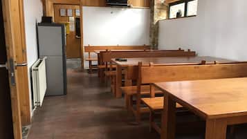 A room with wooden benches and tables, a television mounted on the wall, and a window with a view of the outside.