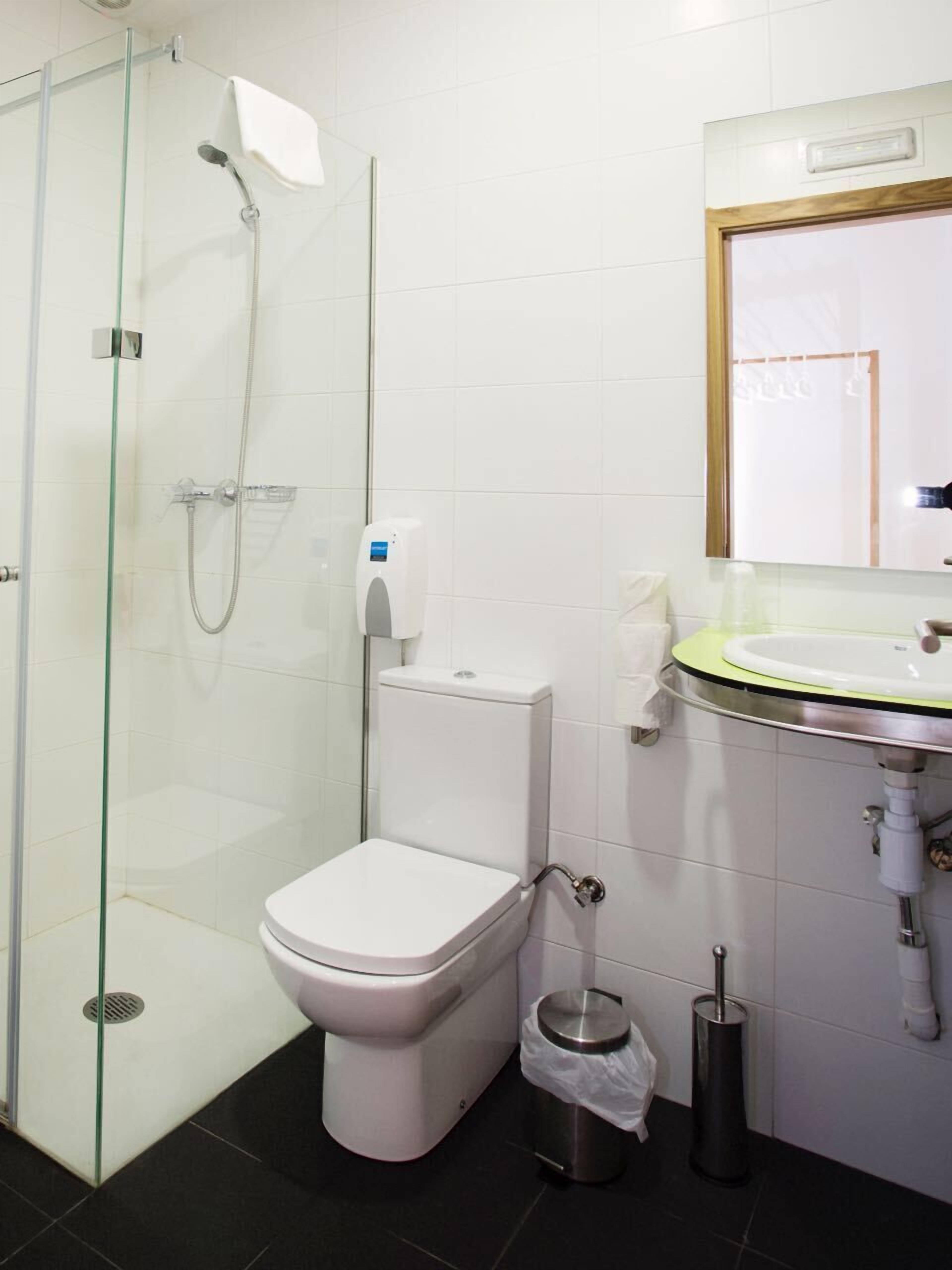 A modern bathroom with a glass-enclosed shower, a white toilet, a sink with a green rim, and a mirror above the sink.