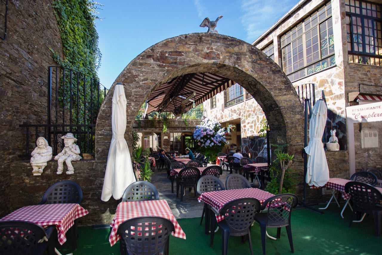 Ein Straßencafé mit steinernen Bögen, Tischen mit karierten Tischdecken und Steinstatuen.