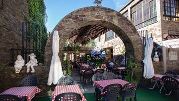 Ein Straßencafé mit steinernen Bögen, Tischen mit karierten Tischdecken und Steinstatuen.