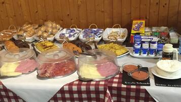 Una mesa de buffet con diversos alimentos, incluyendo carnes, quesos y pasteles, además de bebidas y salsas.