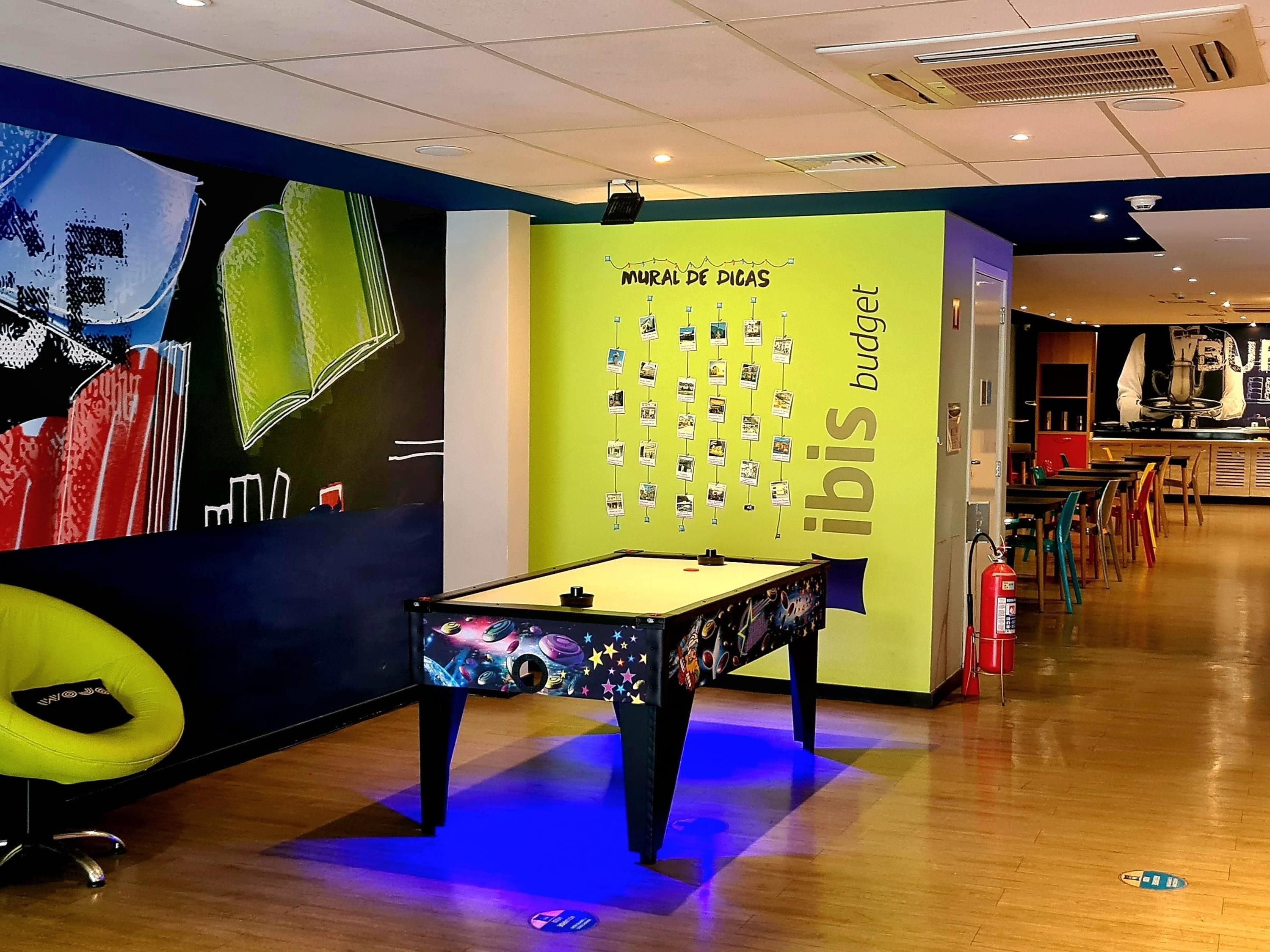 A pool table in a brightly lit room with a wall displaying a 'Mural de Dicas' and a 'bodega' sign.