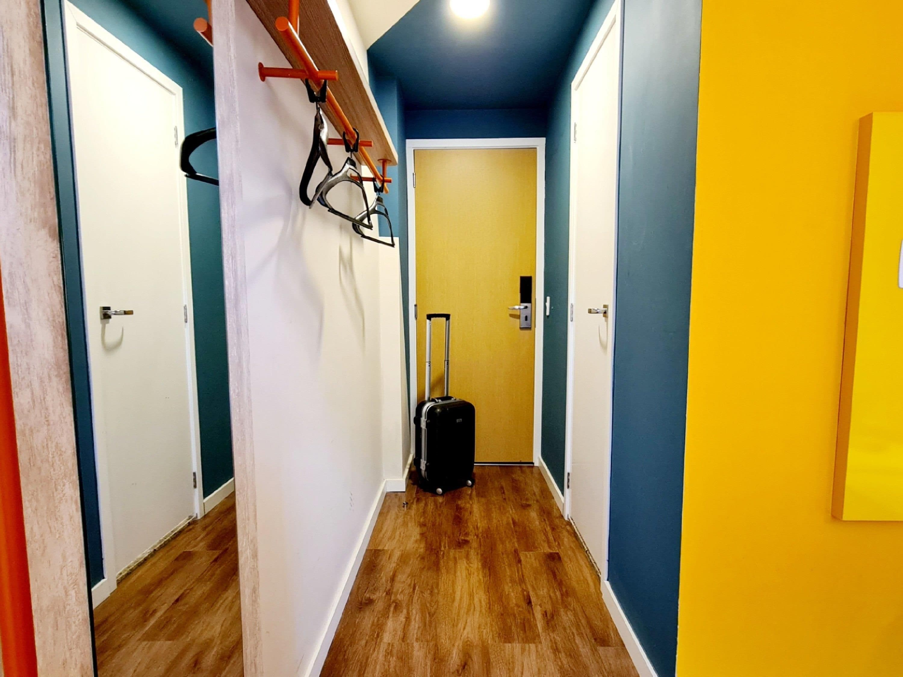 A hallway with wooden flooring, a suitcase, and a door with a handle.