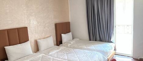 Habitación de hotel con una cama grande, piso de madera, una mesita y una ventana con cortinas.