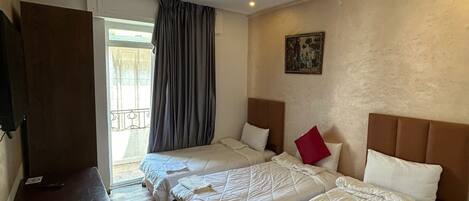 A hotel room with two beds, a wooden floor, a TV, and a painting on the wall.