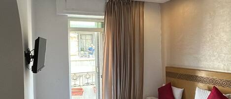 Quarto de hotel com duas camas, televisão, porta que dá para uma varanda e uma cadeira vermelha.