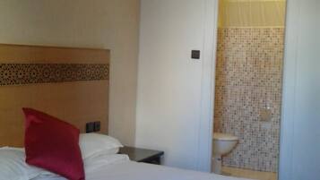 Een hotelkamer met een bed, een nachtkastje en een badkamer, zichtbaar door een open deur.