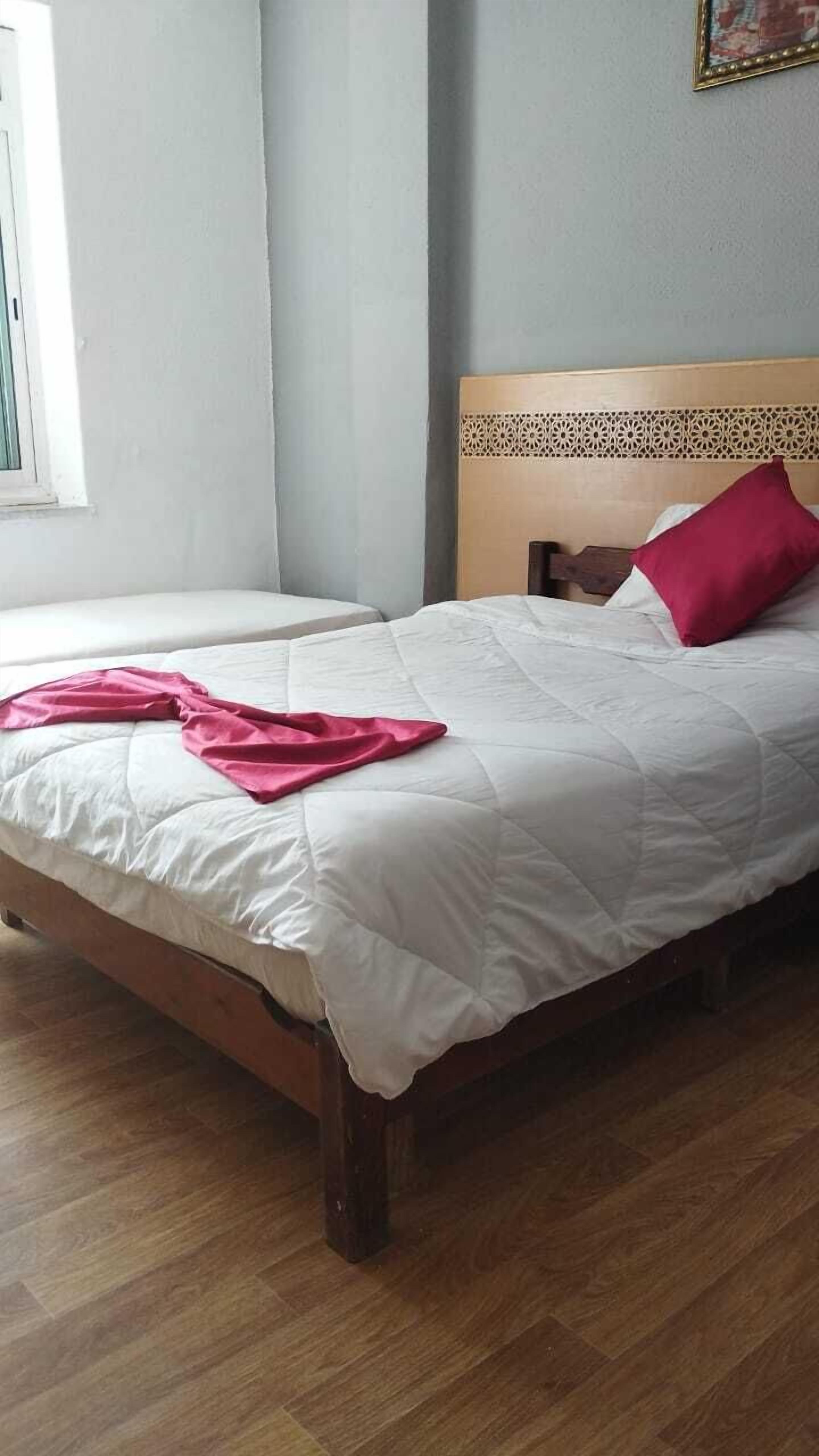 A bedroom with two beds, wooden flooring, a window, and a decorative headboard.