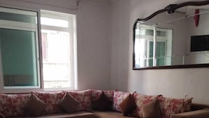 A living room with a sectional sofa, a large window, and a mirror on the wall. - Hotel Astoria (Tangier)