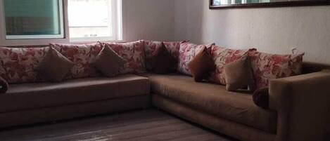 A living room with a sectional sofa, a large window, and a mirror on the wall.