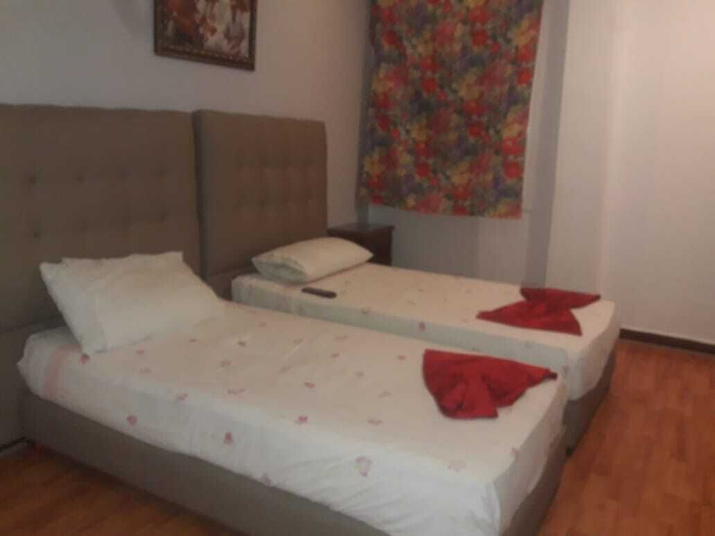 A room with two single beds, a headboard, a nightstand, and a floral tapestry on the wall.